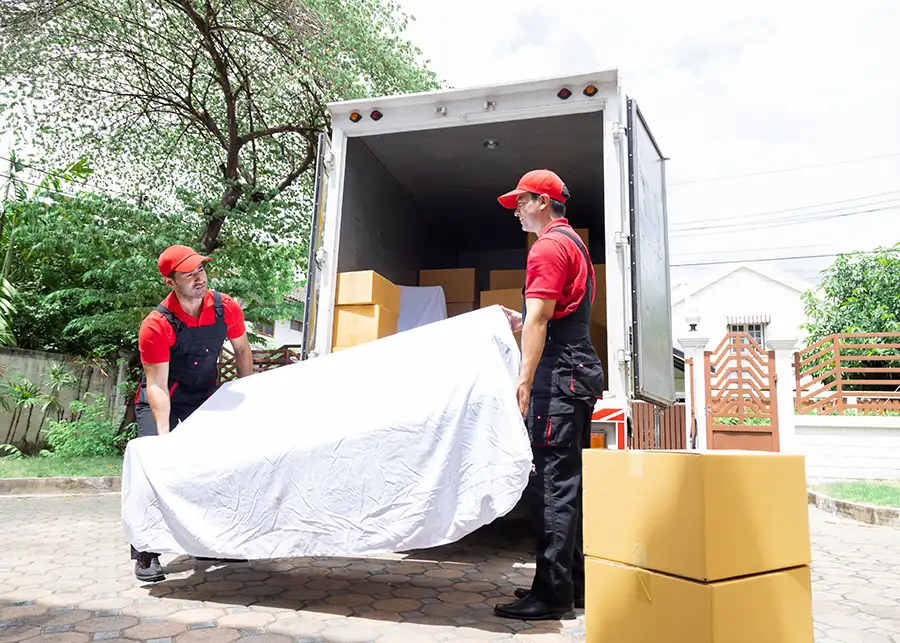 Two Moscardelli Moving & Storage movers in red uniforms carefully unloading furniture from a moving truck at a Springfield IL home