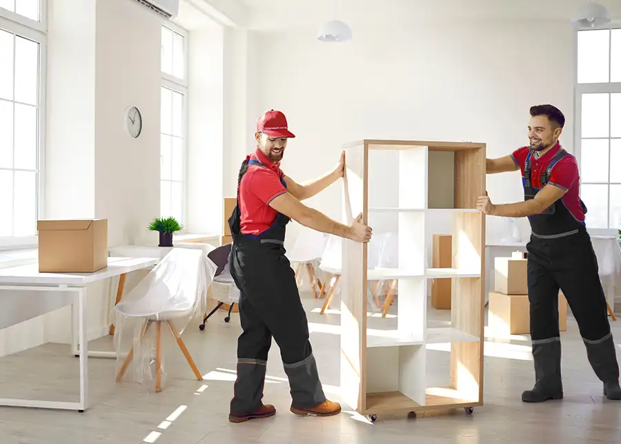 Two Moscardelli Moving & Storage movers smiling as they reposition a wooden shelving unit inside a bright office space in Springfield, IL