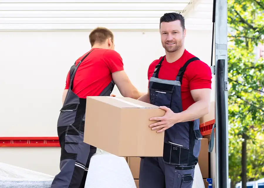 A Moscardelli mover smiling at the camera while passing a heavy cardboard box to a teammate at the back of a moving truck in Springfield, IL
