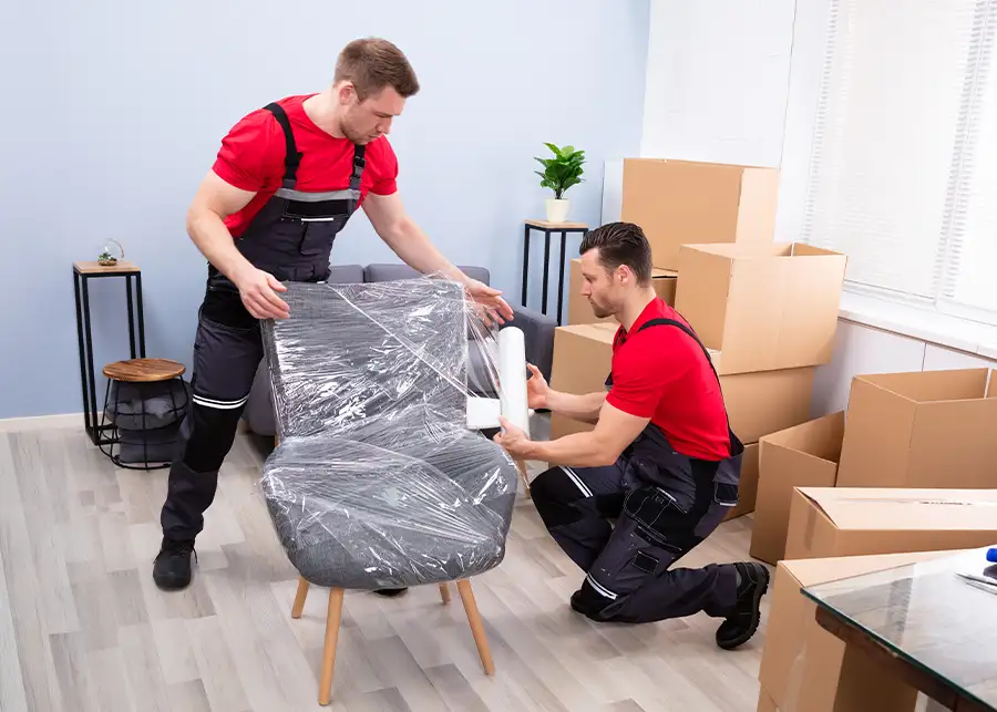 Two Moscardelli Moving & Storage professionals wrapping a chair in protective plastic stretch wrap before loading it for transport in Springfield, IL