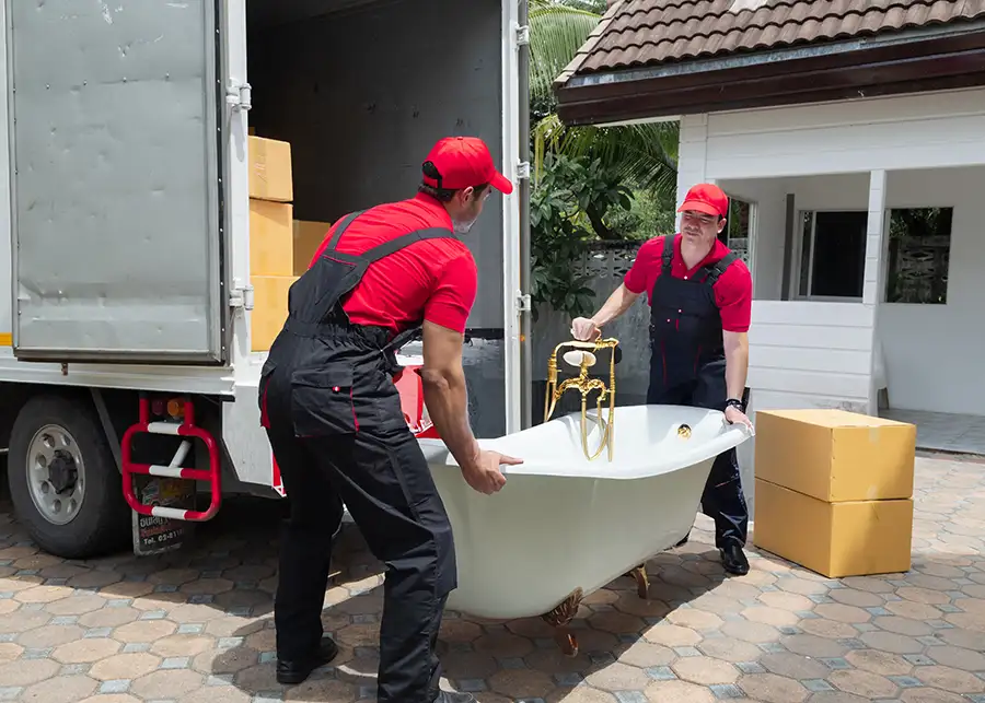 Two Moscardelli Moving & Storage movers in red uniforms carrying a vintage clawfoot bathtub from a moving truck to a Springfield IL home