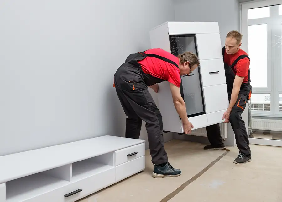Two Moscardelli Moving & Storage professionals in red uniforms carefully reassembling a large entertainment center in an empty room