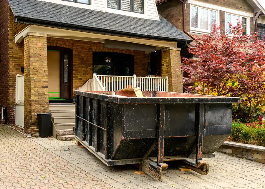 A large black dumpster parked in the brick driveway of a Springfield IL home during a junk removal or estate cleanout service