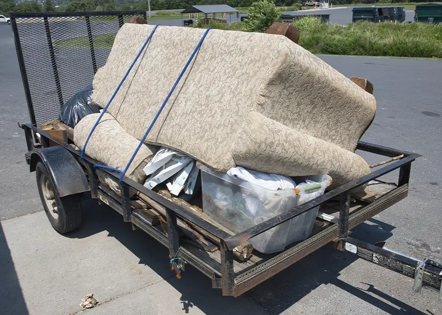 Old furniture and household junk including a sofa and miscellaneous large items loaded on an open utility trailer for haul-away or junk removal